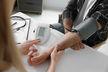 Doctor measuring blood pressure of man at table indoors, closeup