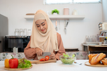 An attractive Asian Muslim woman or housewife in hijab is preparing food in a kitchen