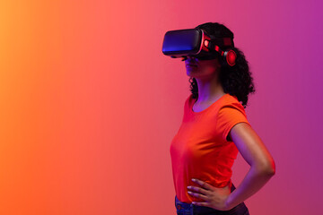 Poster - biracial woman using vr headset on neon pink to orange background