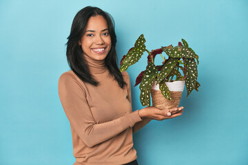 Young Filipina holding a green plant on blue studio backdrop