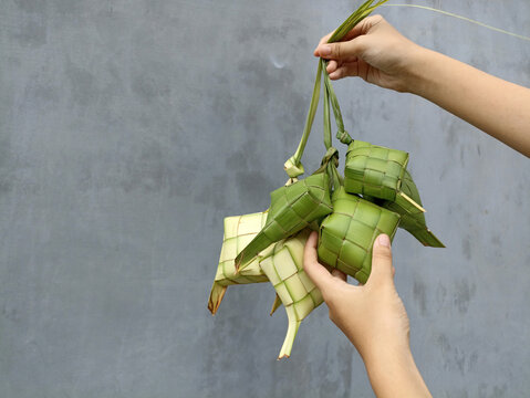 Wall Mural -  - Ketupat (Rice Dumpling) in hands on gray wall background. Ketupat is a natural rice casing made from young coconut leaves for cooking rice during eid Mubarak. Copy space for text card design.