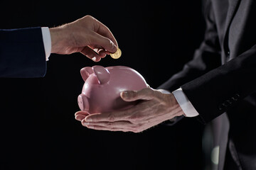 Wall Mural - Hand puts a coin in a piggy bank on a black background