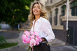 © Svetlana Sokolova - Portrait   of elegant beautiful cheerful  blond woman in  white blouse and silk skirt , holding  pink boquet with pions flowers.  Stylish hand bag and sunglasses.