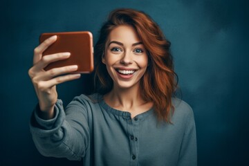 Wall Mural - Medium shot portrait photography of a satisfied girl in her 30s taking a selfie with his mobile against a navy blue background. With generative AI technology