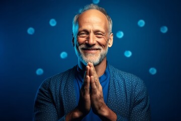 Wall Mural - Lifestyle portrait photography of a satisfied mature man joining palms in a gesture of gratitude against a royal blue background. With generative AI technology