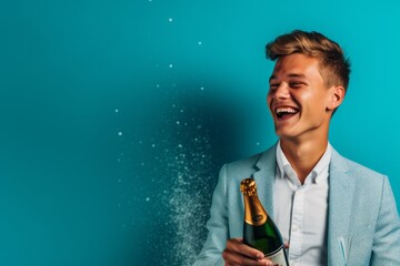 Wall Mural - Lifestyle portrait photography of a happy boy in his 20s uncorking a bottle of champagne against a turquoise blue background. With generative AI technology