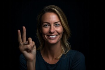 Wall Mural - Headshot portrait photography of a glad girl in her 30s making a peace and love gesture with the fingers against a matte black background. With generative AI technology