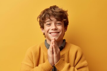 Wall Mural - Close-up portrait photography of a grinning boy in his 20s joining palms in a gesture of gratitude against a pastel yellow background. With generative AI technology
