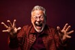 © Markus Schröder - Headshot portrait photography of a happy old man doing loser gesture mocking against a rich maroon background. With generative AI technology