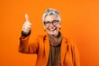 © Markus Schröder - Headshot portrait photography of a joyful mature woman raising both thumbs up against a tangerine orange background. With generative AI technology