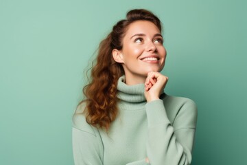 Wall Mural - Medium shot portrait photography of a glad girl in her 20s putting the hand on the chin as if thinking against a pastel green background. With generative AI technology