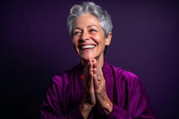 Sticker - Headshot portrait photography of a joyful mature woman joining palms in a gesture of gratitude against a deep purple background. With generative AI technology