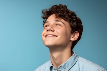 Wall Mural - Medium shot portrait photography of a grinning boy in his 20s putting the hand on the forehead to look for someone in the distance against a sky-blue background. With generative AI technology