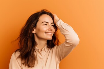 Poster - Lifestyle portrait photography of a glad girl in her 30s putting the hand on the forehead to look for someone in the distance against a pastel orange background. With generative AI technology