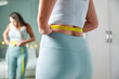 © dragonstock - Young woman taking measurements of her body in front of the mirror in her bedroom