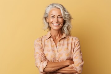 Poster - Medium shot portrait photography of a happy mature woman crossing the arms against a beige background. With generative AI technology