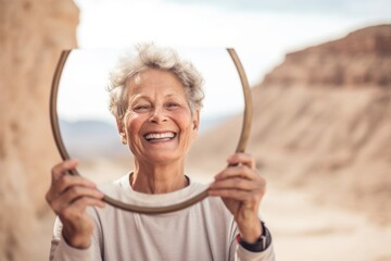 Poster - Close-up portrait photography of a joyful mature woman holding a mirror wearing a comfortable yoga top at the masada in southern district israel. With generative AI technology