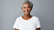 Cheerful mature African American woman with grey hair in casual clothes with a genuine smile on gray background, lookinh at camera in the studio