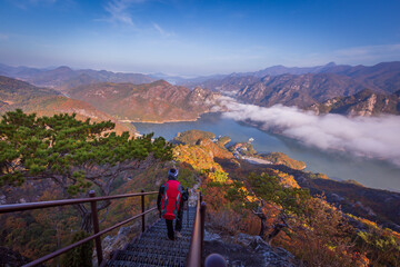 tourist with backpack admiring landscape in Autumn In the morning, a sea of ​​mist flows through the river in the valley In the autumn at Jebibong of Waraksan Mountain National Park, South Korea.