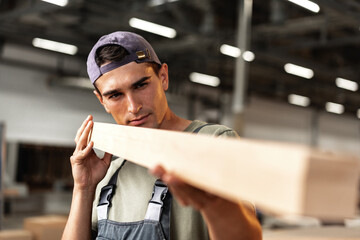 Wall Mural - Young carpenter man looking and choosing wood plank at workshop in carpenter wood factory