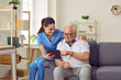 © Studio Romantic - Nurse shows older male patient digital tablet with new software application for health monitoring or patient's health test laboratory results. Female nurse and senior man sitting on couch in room.
