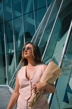 Chic In The City: Model Glides In Pink Dress, Sunglasses, Amidst Blue Glass Facades