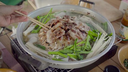 Wall Mural - Korean BBQ with sliced pork and vegetable soup, People hand using chopsticks grilled dinner the family. picnic outdoor