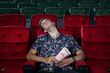© charnsitr - Man sleeping in a movie theatre while watching moviewith popcorn in his hand