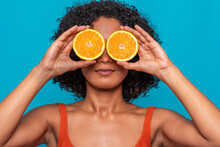 Serious Ethnic Woman Covering Eyes With Orange Slices In Blue Studio