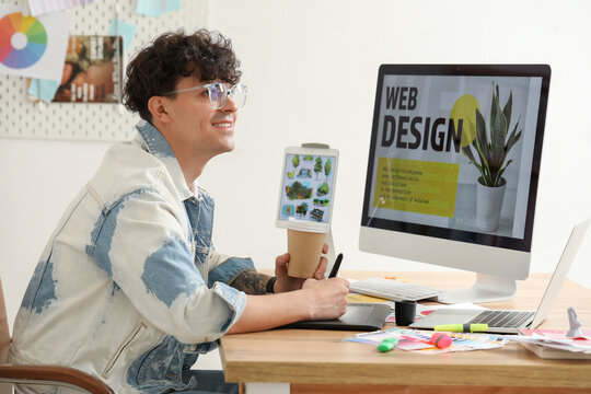 Male graphic designer with cup of coffee working at table in office