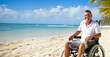 Handicapped or disabled man in a wheelchair, enjoying the sun on a beach. Shallow field of view with copy space.