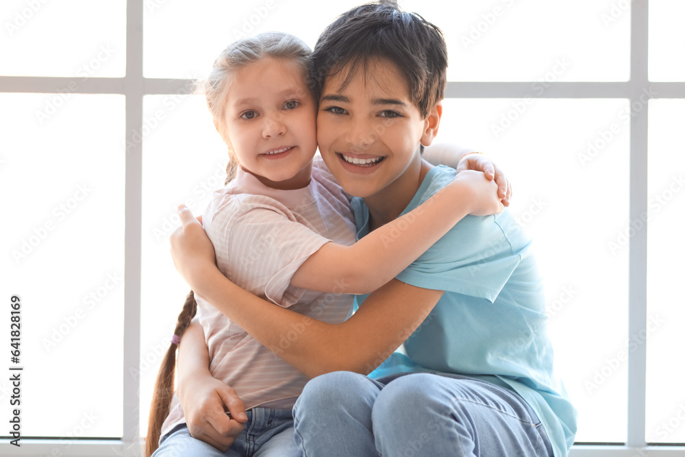 Little boy with his sister hugging near window