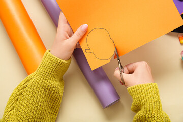 Woman cutting pumpkins out of paper for Halloween on beige background