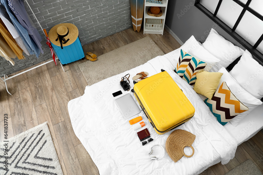 Interior of bedroom with suitcase and summer accessories on bed