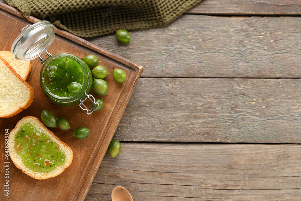 Jar with tasty gooseberry jam and bread on wooden background