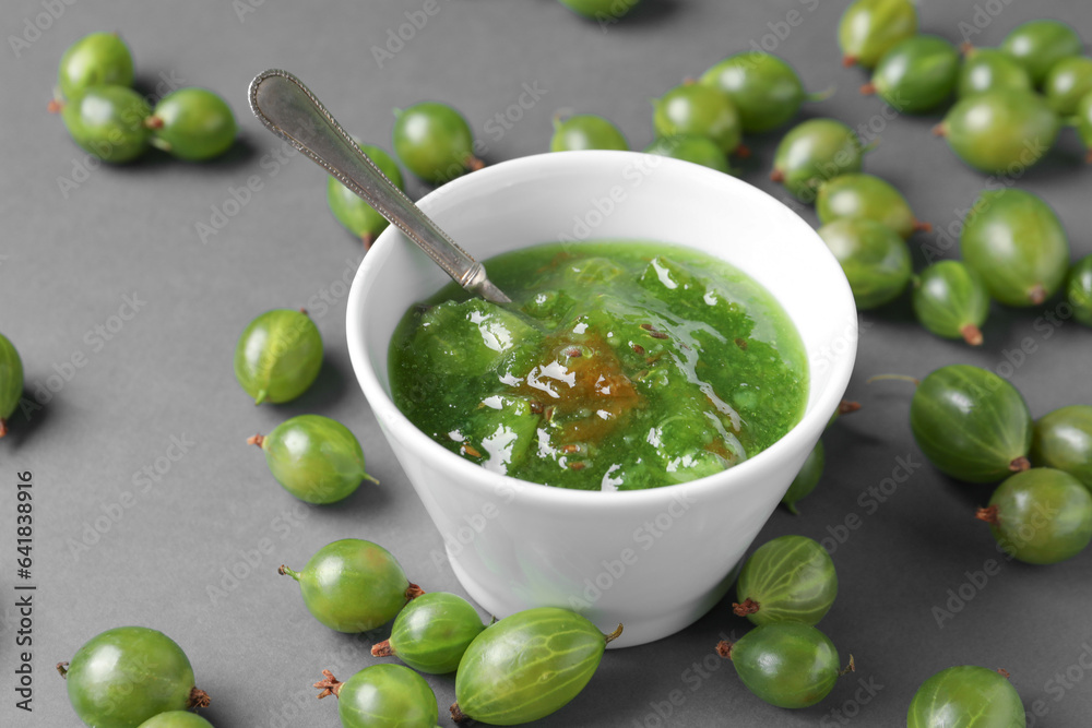 Bowl with tasty gooseberry jam and fresh berries on grey background