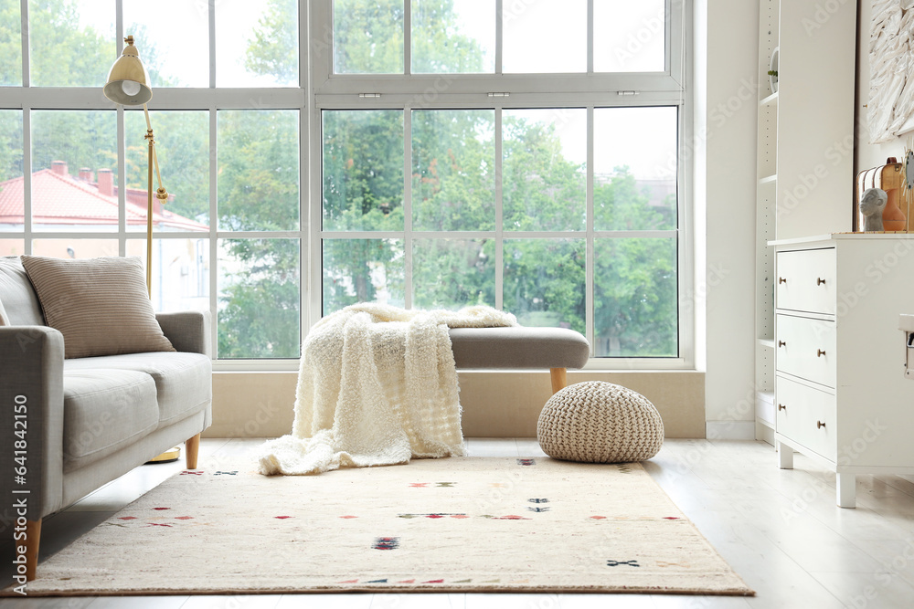 Soft bench with plaid and pouf near window in living room