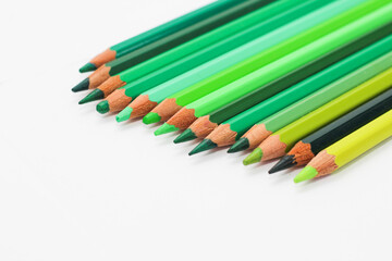 Wall Mural - Multi-colored pencils lie on a white table, the green range of colors