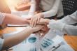 © Satori Studio - Positive diverse business team putting their hands on top of each other, showing unity and teamwork