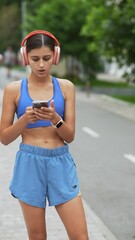 Wall Mural - Running through her route, a girl in athletic clothing and headphones looks at her smartphone