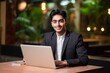 © The Little Hut - Generative AI : Close-up photo. Portrait of a young Indian student wearing a suit studying online. He looks at the camera with a smile.