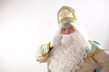 Place For Text On A White Background A Man In Costume Of St. Nicholas Drinks Tea From A White Cup Sinterklaas Portrait. USA On A White Background. Dutch Santa Claus St Nicholas Christmas New Year