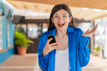 Wall Mural - Young pretty woman at outdoors using mobile phone while doing thumbs up