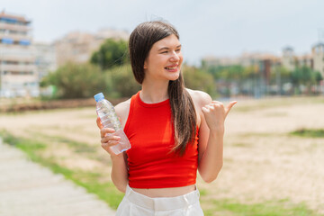 Wall Mural - Young pretty Ukrainian woman with a bottle of water at outdoors pointing to the side to present a product