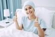 © amnaj - Female cancer patient lying on a hospital bed. Cheerful woman cancer patient giving thumbs up looking at camera.