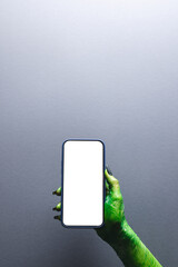 Poster - Vertical image of green monster hand holding smartphone with copy space on grey background