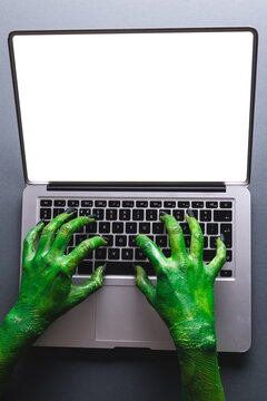Vertical image of green monster hands writing on laptop with copy space on grey background
