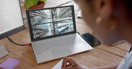 Poster - African american female security officer watching warehouse cctv camera views on laptop, slow motion