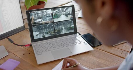 Poster - African american female security officer watching business cctv camera views on laptop, slow motion