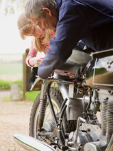 Young girl helping grandfather repairing motorbike

